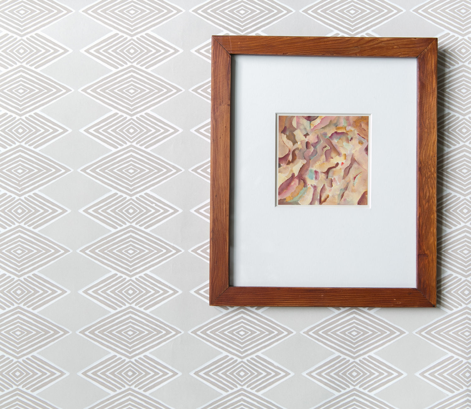 A framed abstract art print with a white mat and a medium brown wooden frame, displayed against a light gray and white geometric patterned wallpaper.