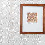 A framed abstract art print with a white mat and a medium brown wooden frame, displayed against a light gray and white geometric patterned wallpaper.