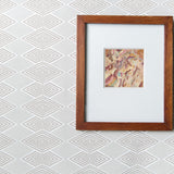 A framed abstract art print with a white mat and a medium brown wooden frame, displayed against a light gray and white geometric patterned wallpaper.