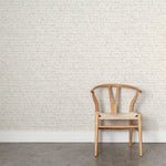 Angled wooden chair with woven seat on concrete floor against wallpaper in a watercolor broken stripe pattern in soft beige. 