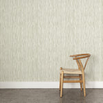 A wooden chair stands in front of a wall papered in a painterly stripe pattern in sage on a white field.