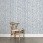 A wooden chair stands in front of a wall papered in a painterly stripe pattern in navy on a white field.