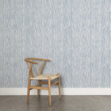 A wooden chair stands in front of a wall papered in a painterly stripe pattern in navy on a white field.