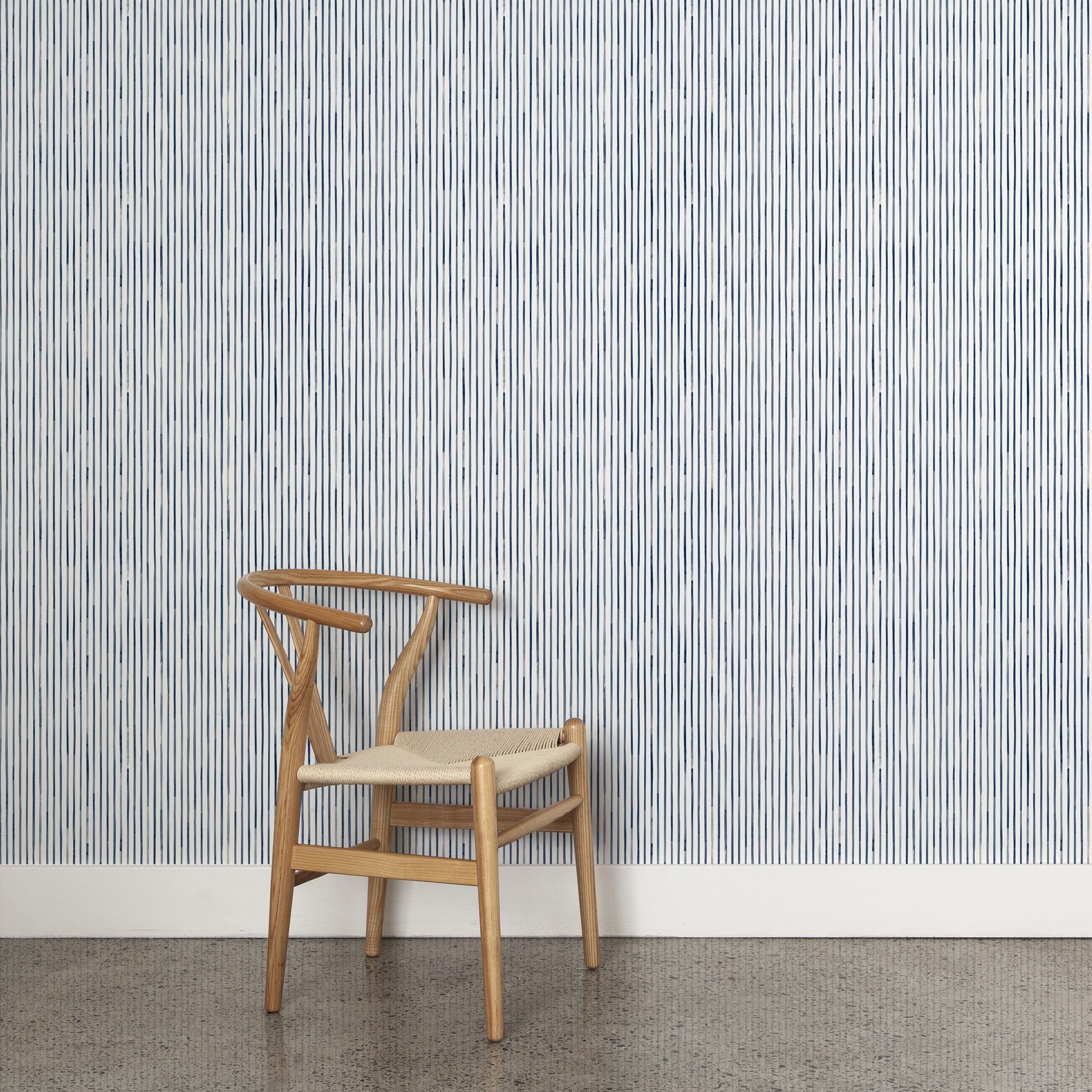 A wooden chair stands in front of a wall papered in a painterly stripe pattern in navy on a white field.