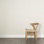 A wooden chair stands in front of a wall papered in a painterly grid pattern in gray on a white field.
