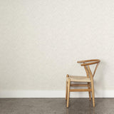 A wooden chair stands in front of a wall papered in a painterly grid pattern in gray on a white field.