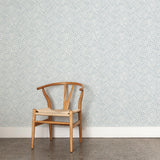 A wooden chair stands in front of a wall papered in a painterly grid pattern in navy on a white field.