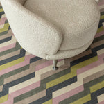 White bouclé side chair atop a handwoven rug with a stacked zig zag stripe in purple, lime green, cream and shades of grey. 