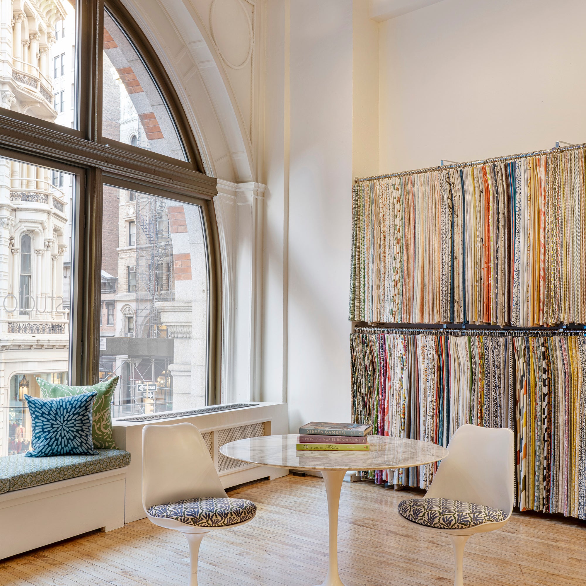 Interior design showroom with a curved glass window looking over Manhattan, and seats in front of a wall of fabric swatches.