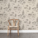 A wooden chair stands in front of a wall papered in a painterly shrub and tree print in charcoal on a cream field.