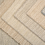 A close-up of overlapping woven rug samples in neutral tones, including beige, cream, tan, and a muted blue-gray, showing the texture and pile of the rugs.