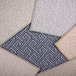 Stack of broadloom carpet samples with a Greek key motif in neutral colors. 