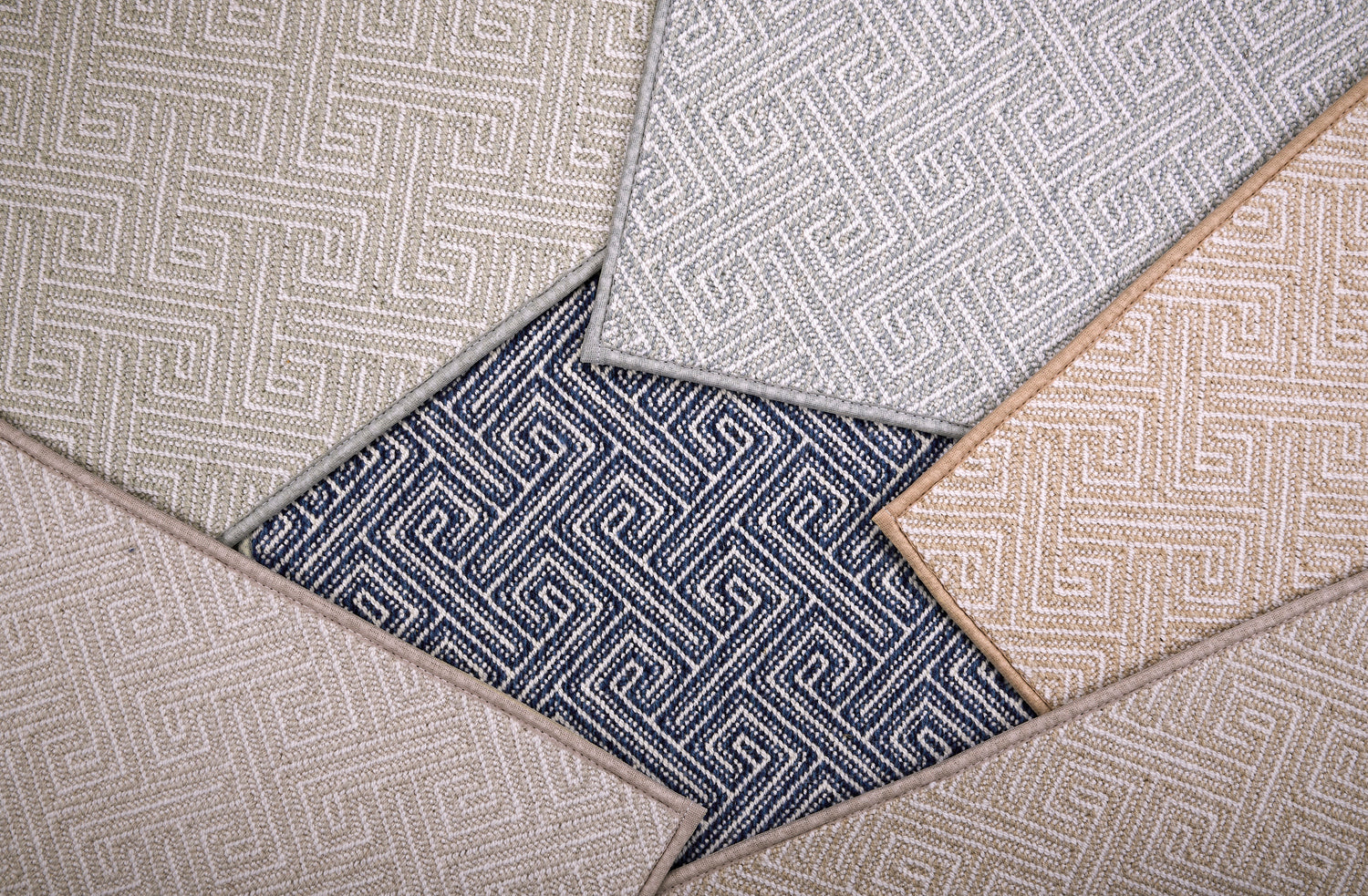 Stack of broadloom carpet samples with a Greek key motif in neutral colors. 