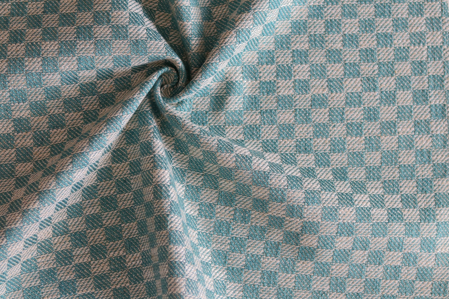 Close up of draped woven fabric with small scale checkerboard pattern in white and turquoise. 