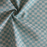 Close up of draped woven fabric with small scale checkerboard pattern in white and turquoise. 