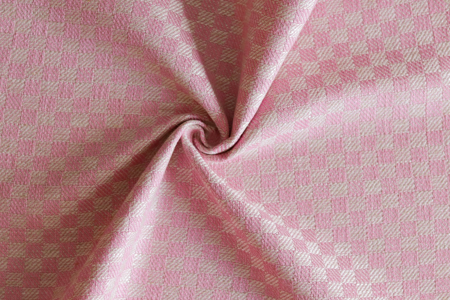 Close up of draped woven fabric with small scale checkerboard pattern in white and bright pink. 