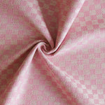 Close up of draped woven fabric with small scale checkerboard pattern in white and bright pink. 