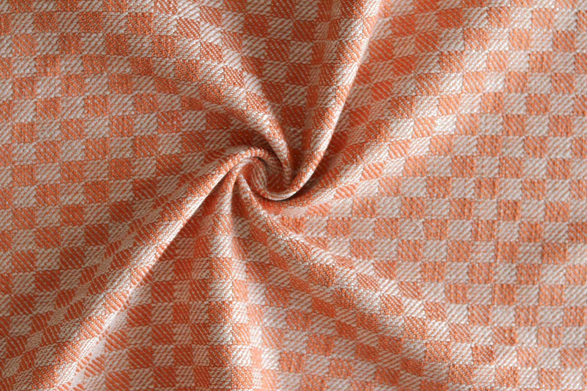 Close up of draped woven fabric with small scale checkerboard pattern in white and bright orange. 
