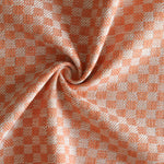 Close up of draped woven fabric with small scale checkerboard pattern in white and bright orange. 