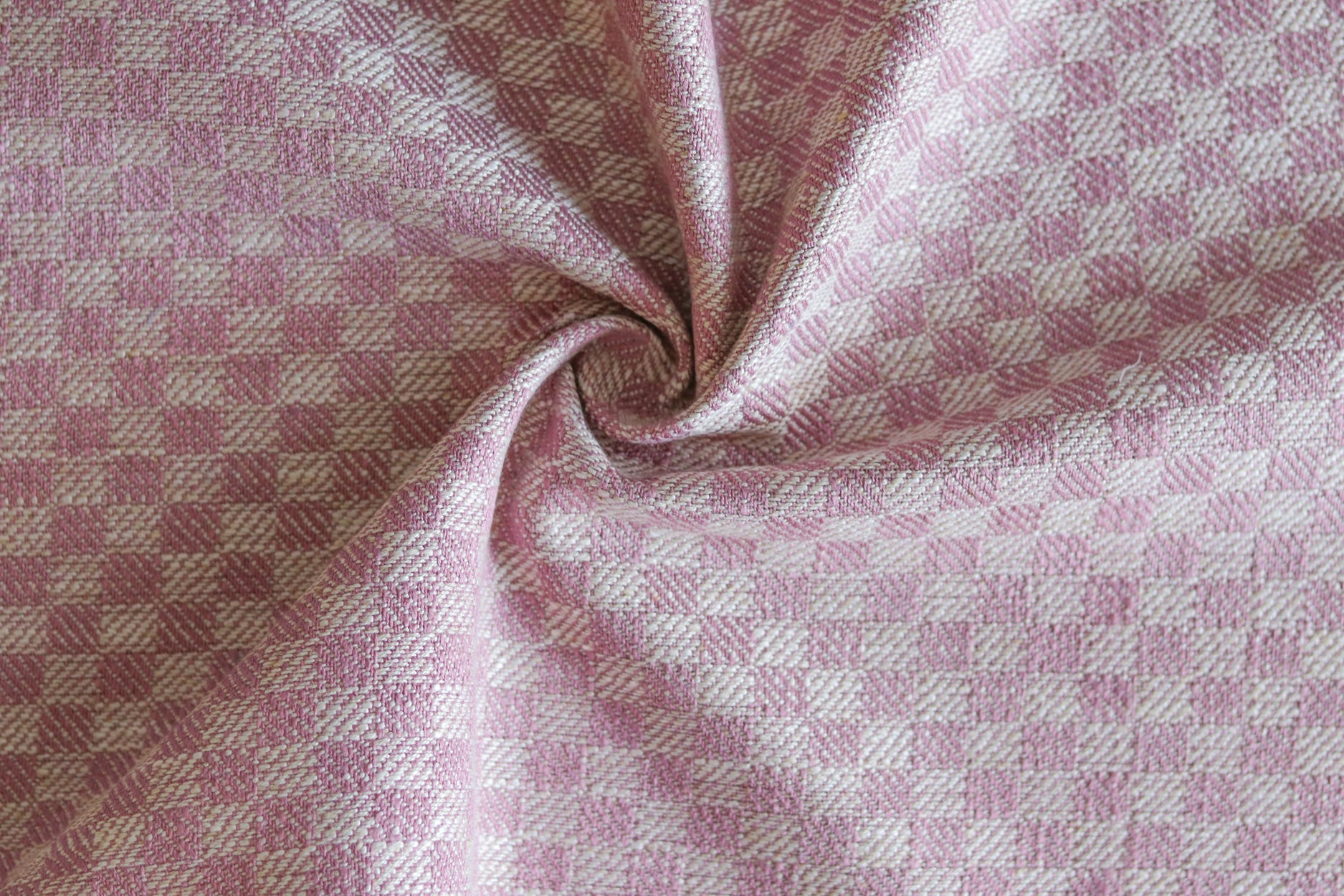 Close up of draped woven fabric with small scale checkerboard pattern in white and bubble gum pink.