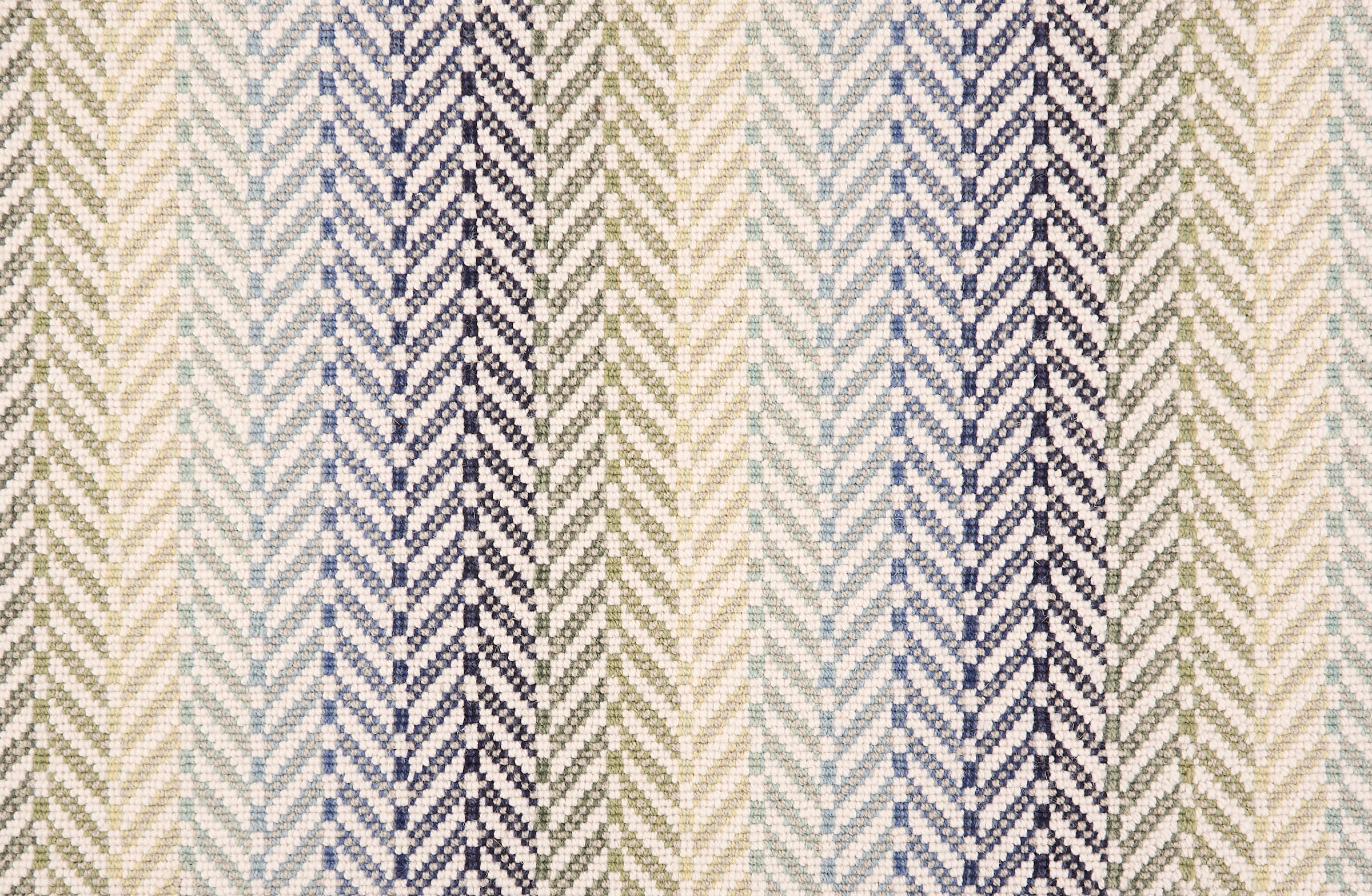 Broadloom carpet in a herringbone pattern with ombré stripe design in navy, blue, green and yellow with white. 