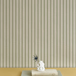 A stack of booked with a vase and thistle, against a wallpaper playful hand drawn dotted stripe in soft green.