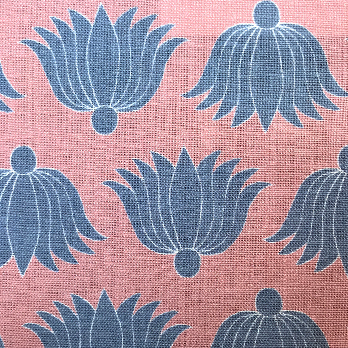 Detail of fabric in a repeating lotus print in blue and white on a coral field.