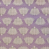 Detail of fabric in a repeating lotus print in cream and tan on a light purple field.