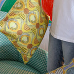 Woman in white tee shirt and jeans standing holding printed geometric pillows against a green checkerboard patterned arm chair.