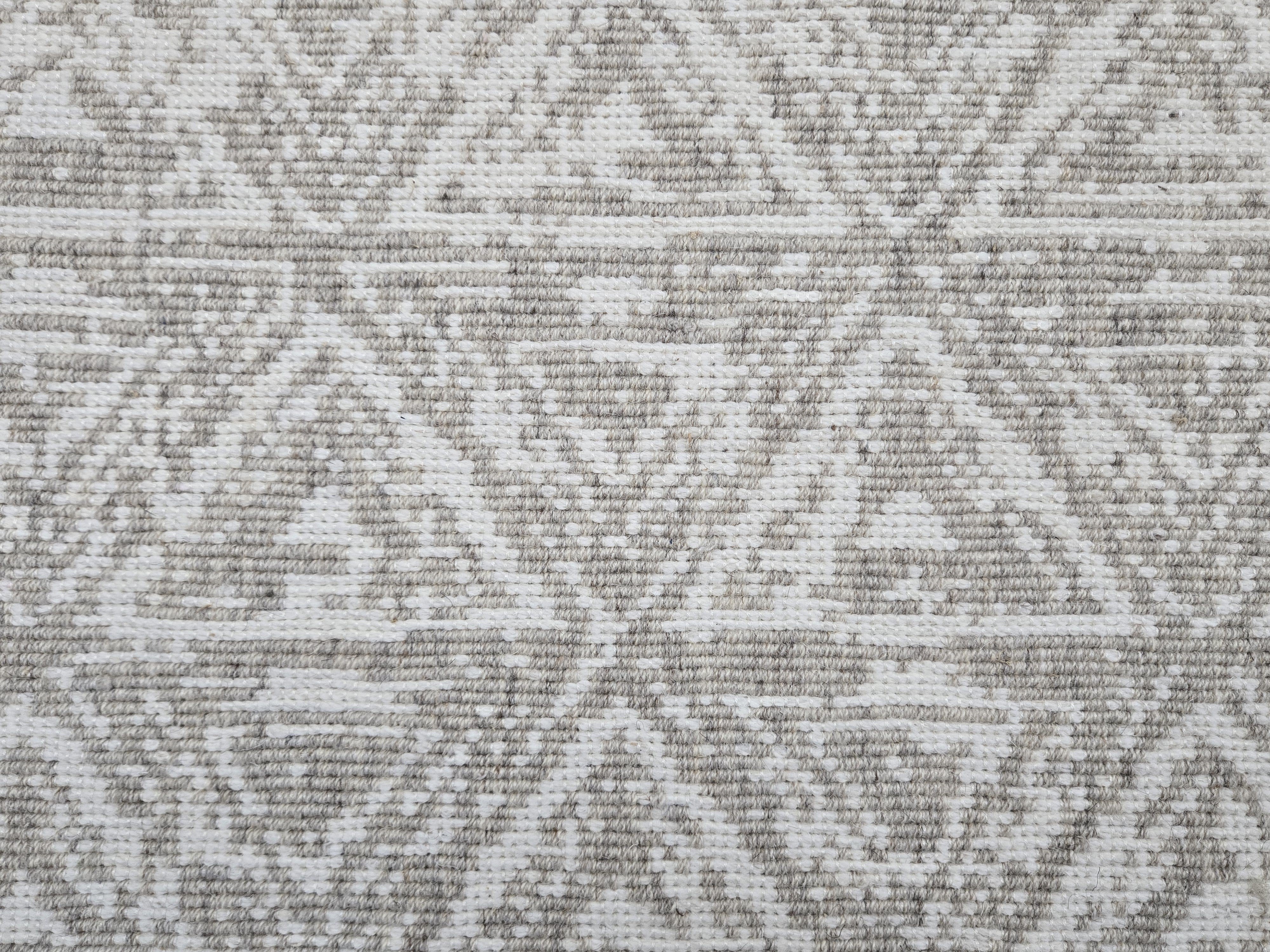 Broadloom carpet sample in a textural stacked triangle pattern in white and taupe.