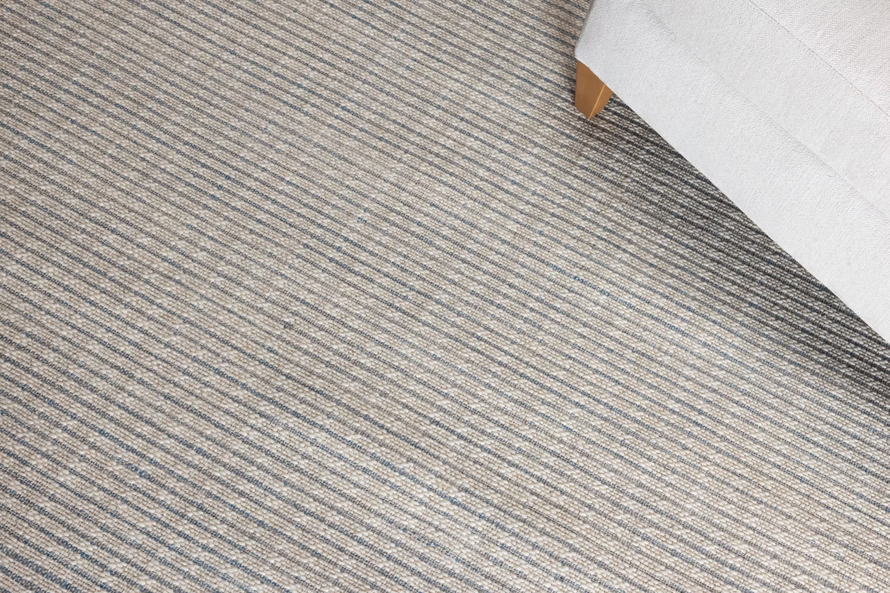 Close-up of a textured striped gray carpet with a white chair corner. 