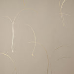 Detail of a wallpaper in an elongated paint splatter pattern in metallic gold on a cream field.