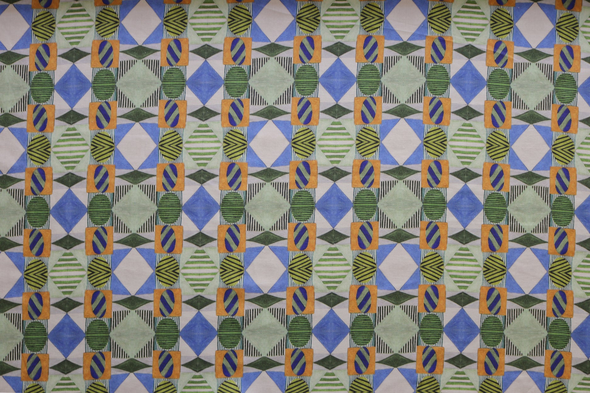 Close up of printed fabric with collaged pattern with striped and solid diamonds, squares and ovals in blue, green, orange and white. 