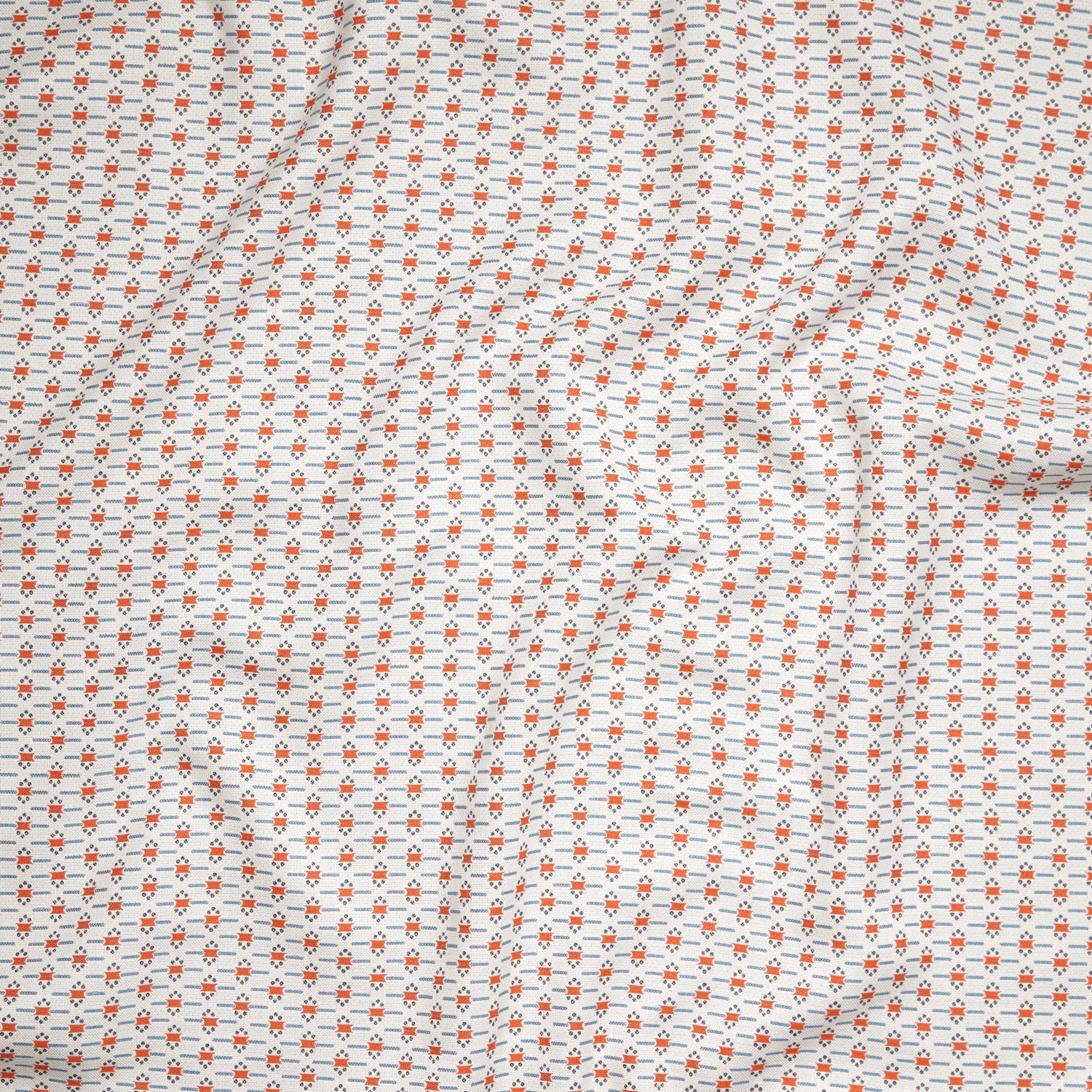 Close up of gently draped woven Indoor-Outdoor fabric with small scale geometric ditsy print in coral and light blue on white. 