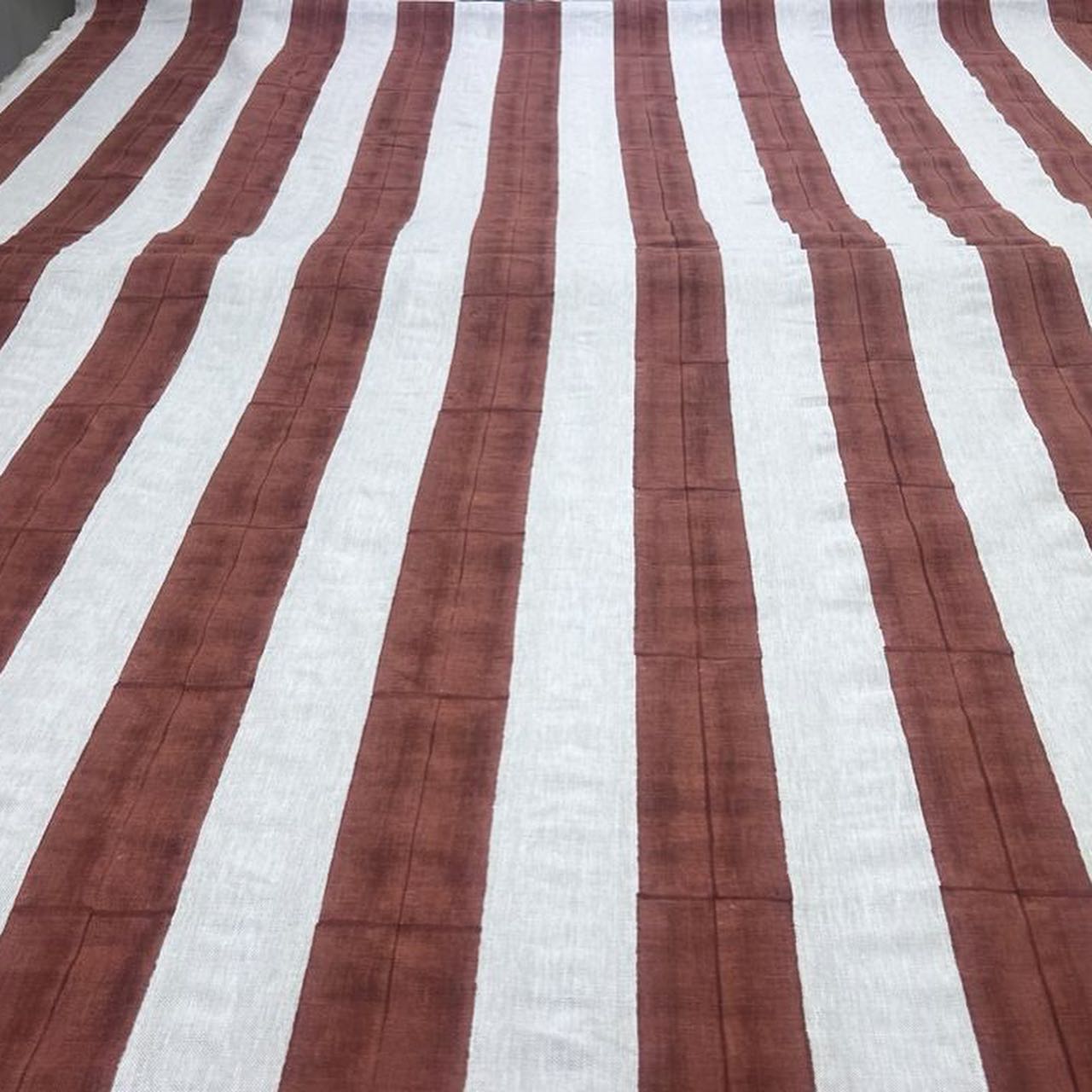 Overhead image of a fabric in a wide stripe pattern in rust and cream layed flat on a table. 