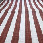 Overhead image of a fabric in a wide stripe pattern in rust and cream layed flat on a table. 