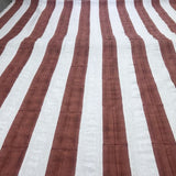 Overhead image of a fabric in a wide stripe pattern in rust and cream layed flat on a table. 