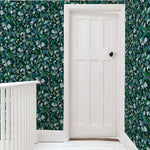 A door stands at the end of a hallway papered in a minimal leaf print in shades of blue, green and navy.