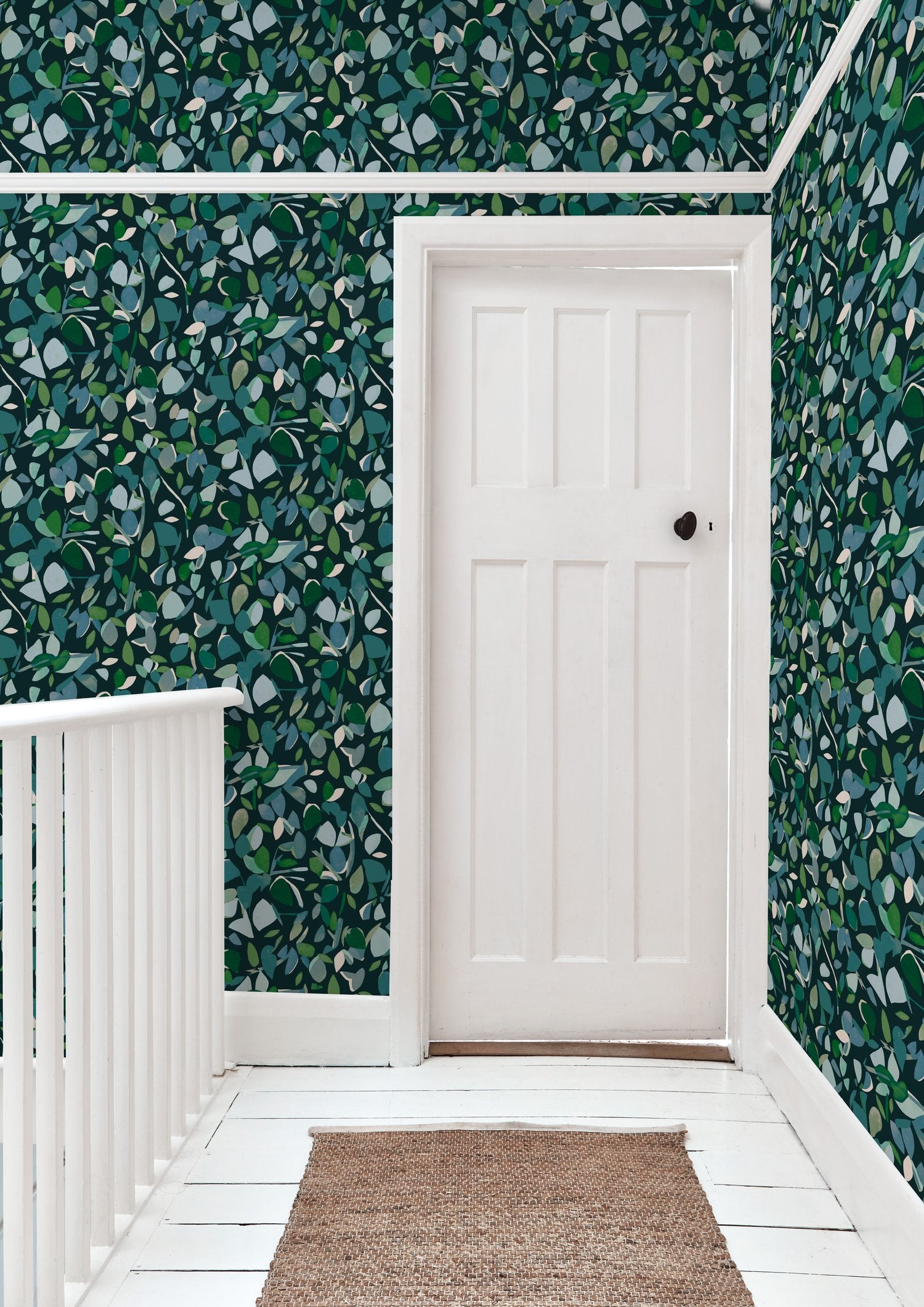 A door stands at the end of a hallway papered in a minimal leaf print in shades of blue, green and navy.