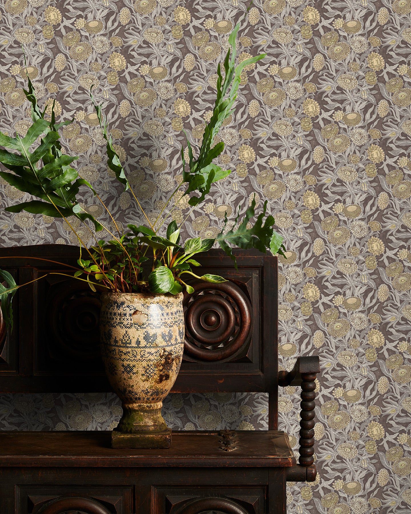 Decorative wallpaper with brown floral pattern, wooden cabinet with plants, and ornate vase.