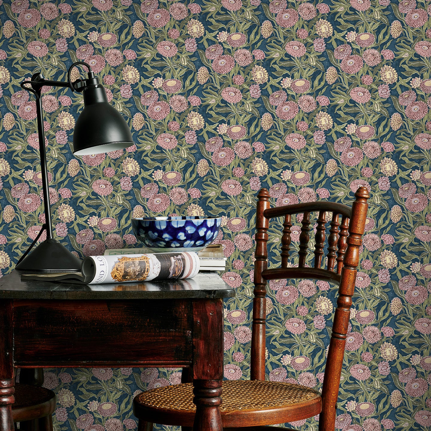 Room interior with pink and blue floral wallpaper, wooden chair, and desk lamp.