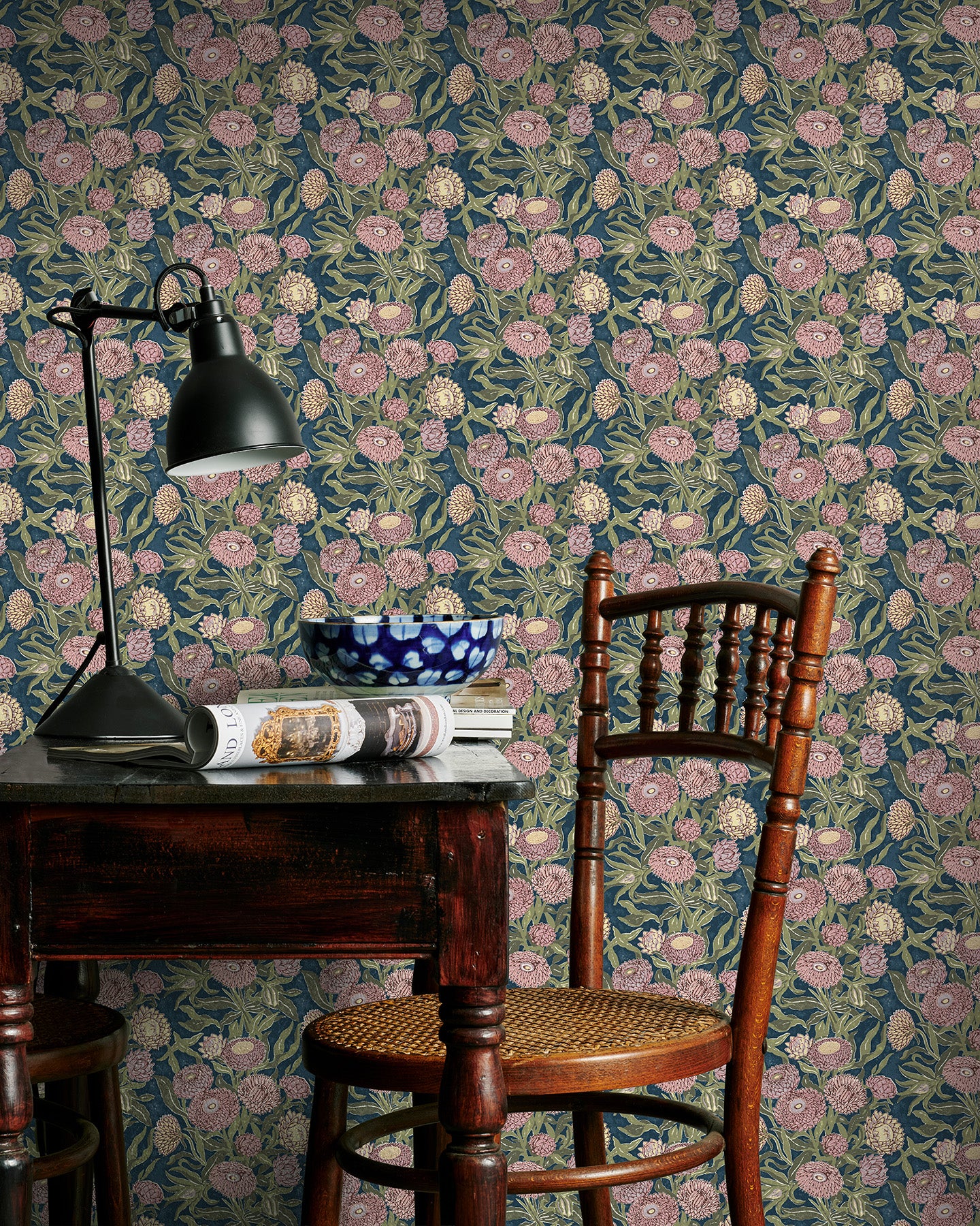 Room interior with pink and blue floral wallpaper, wooden chair, and desk lamp.