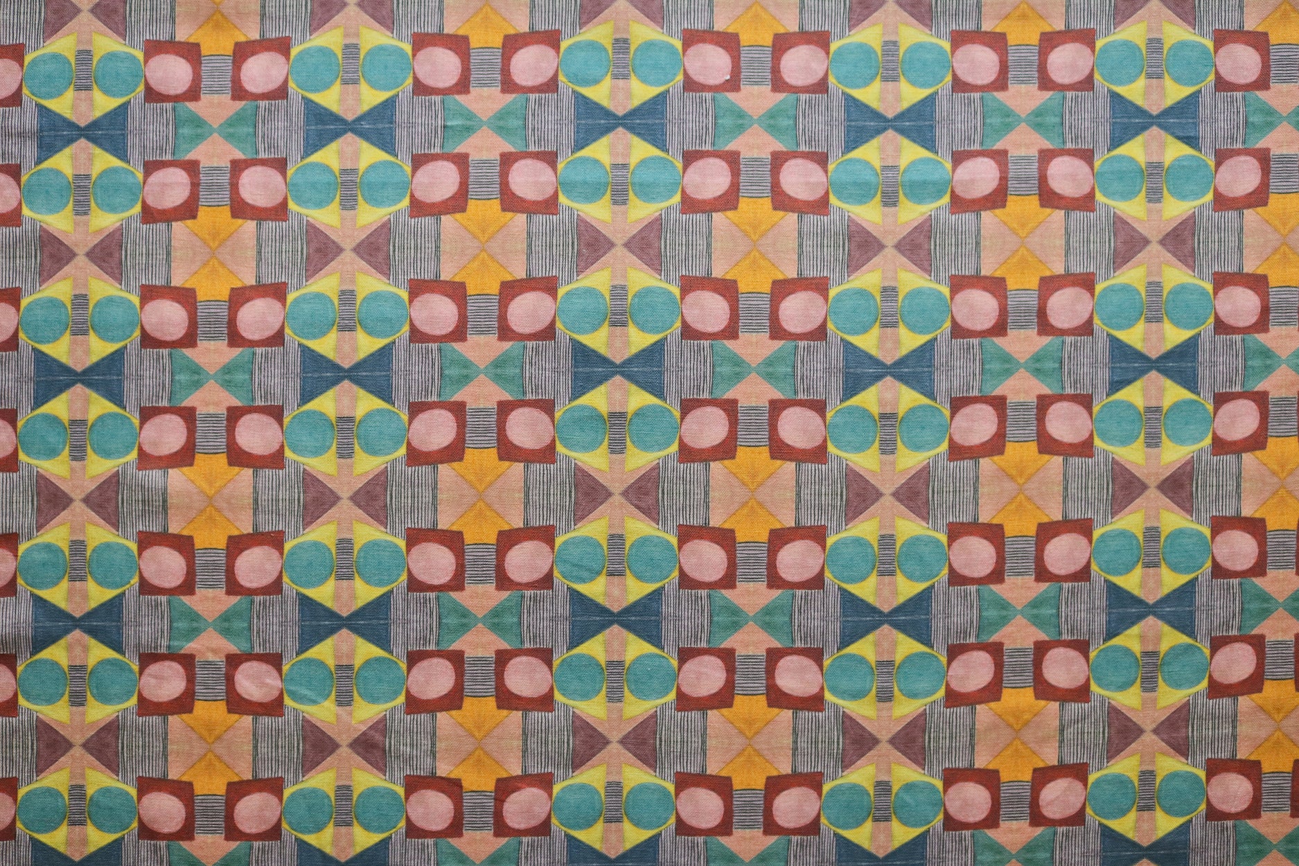 Close up of printed fabric with a complex geometric pattern with pink, red, blue, yellow, orange and turquoise.