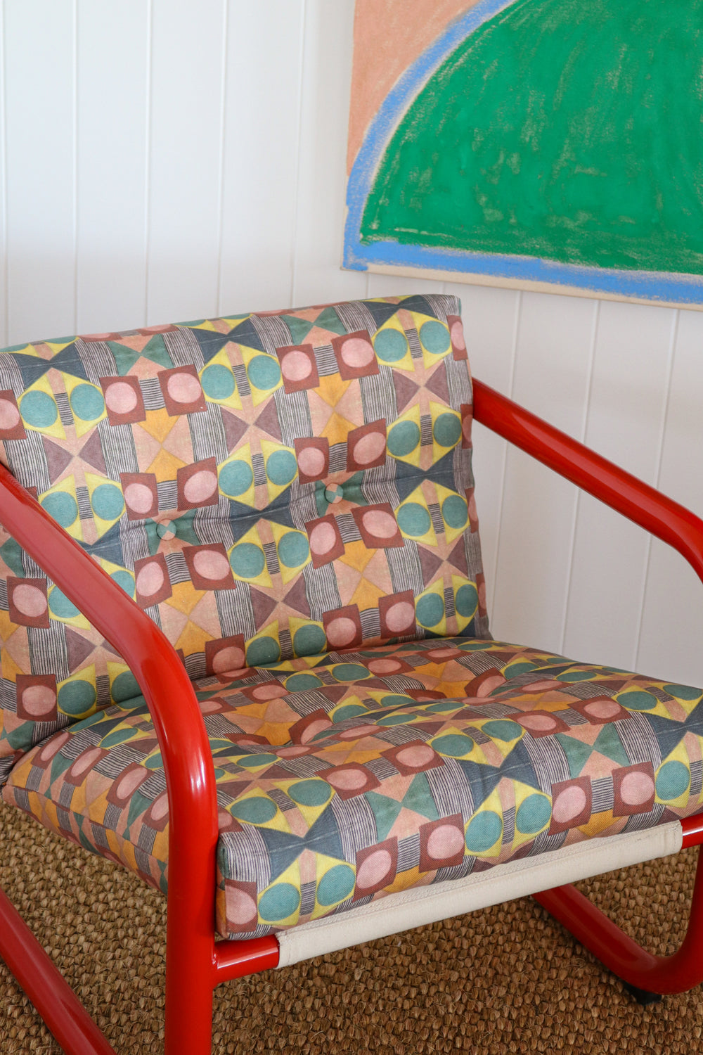 Red metal frame side chair with bold geometric print upholstery against a white paneled wall and bold geometric drawing. 