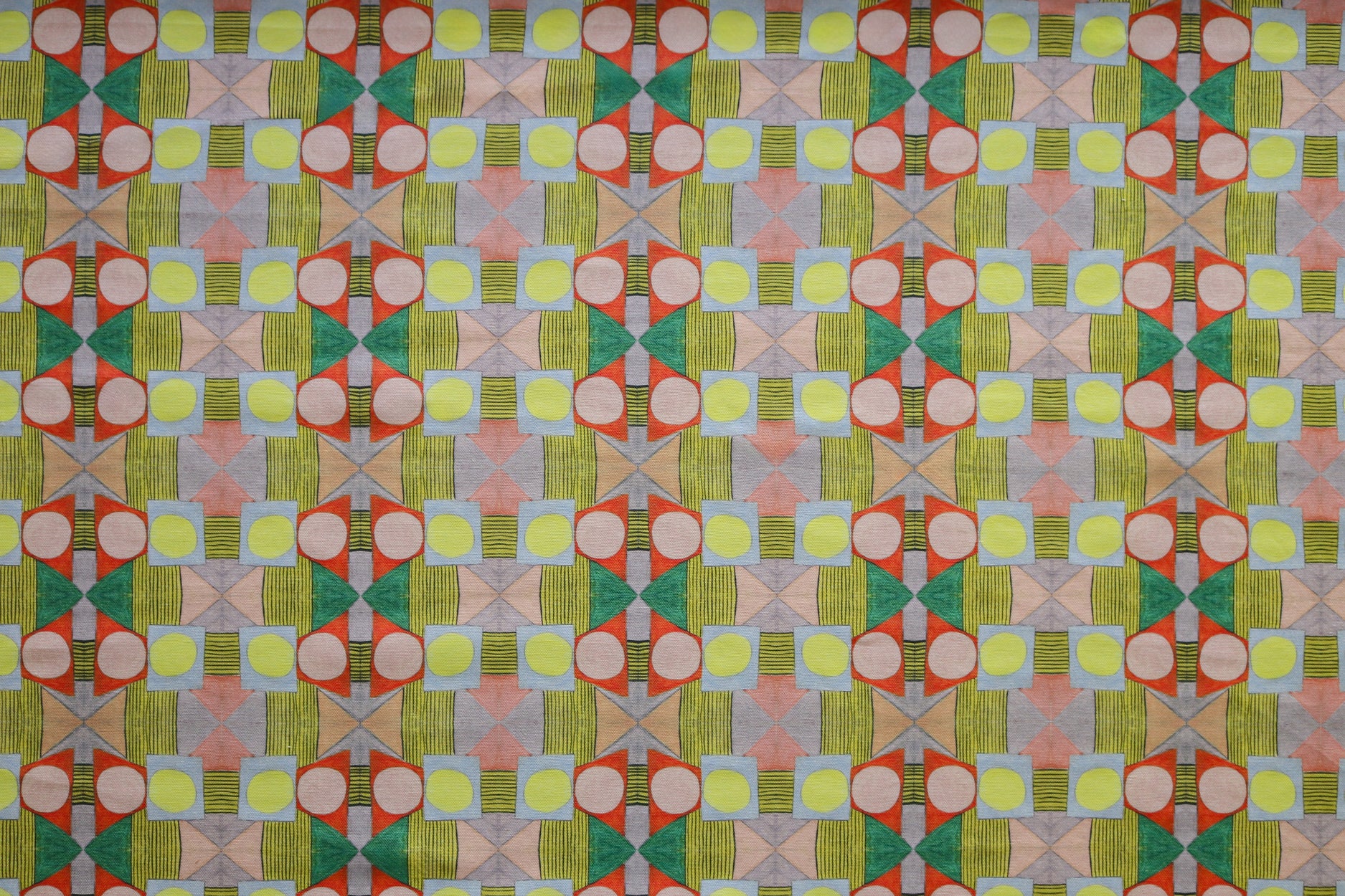 Close up of printed fabric with a complex geometric pattern with pink, red, light purple, green and yellow. 