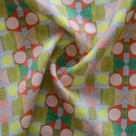 Close up of gently draped printed fabric with a complex geometric pattern with pink, red, light purple, green and yellow. 