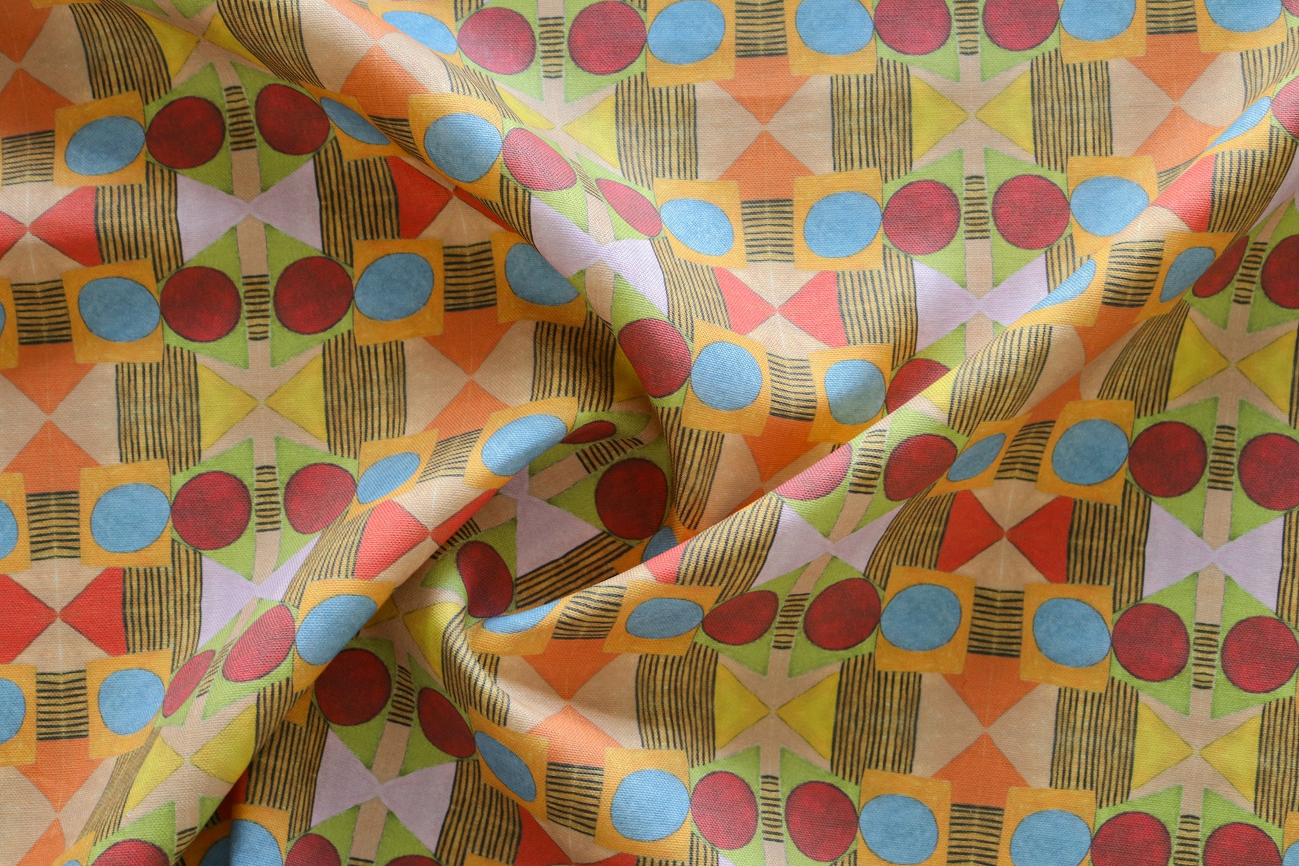 Close up of gently draped printed fabric with a complex geometric pattern with red, blue, orange and green. 