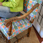 Detail of a seated woman in lime green cardigan and jeans on an ornate wooden side chair with geometric patterned upholstery.