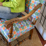 Detail of a seated woman in lime green cardigan and jeans on an ornate wooden side chair with geometric patterned upholstery.
