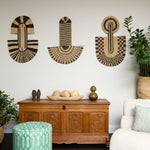 Living room scene with three black and tan sculptural woven panels, ornately carved wooden chest, baskets with house plans, white upholstered side chair and a stripe patterned footstool in green.